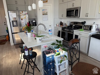 Kitchen with light wood finished floors, a breakfast bar, light countertops, decorative backsplash, and appliances with stainless steel finishes