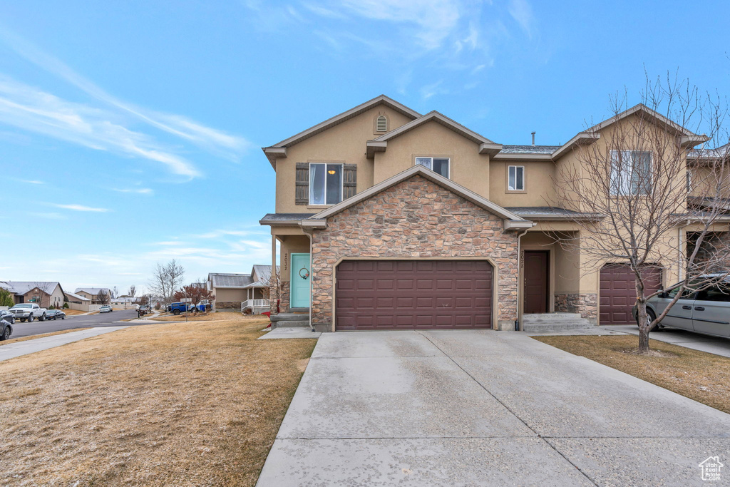 Traditional home featuring stone siding, stucco siding, driveway, and a garage