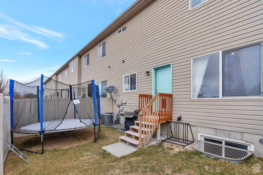 Back of house featuring central air condition unit, a trampoline, a lawn, and fence