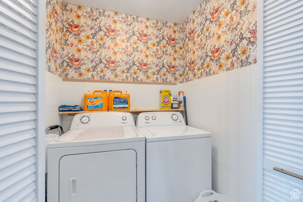 Laundry area featuring wallpapered walls, washing machine and clothes dryer, a textured ceiling, and wainscoting