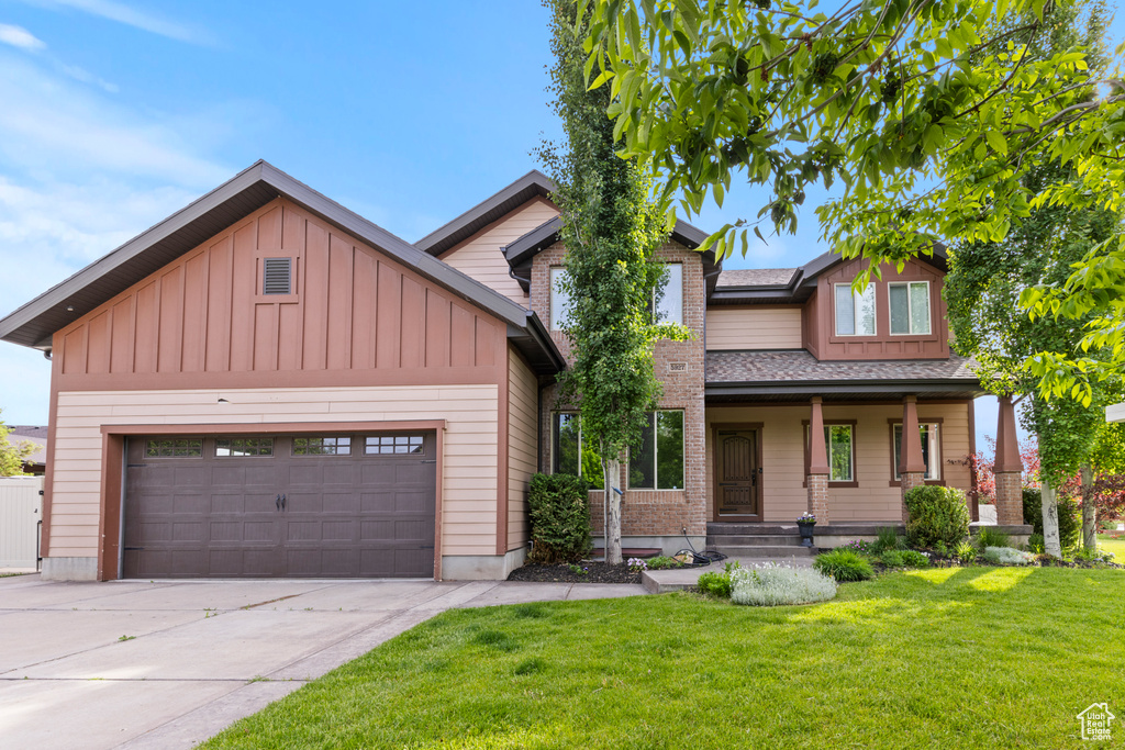 Craftsman-style home featuring board and batten siding, concrete driveway, a front lawn, an attached garage, and a porch