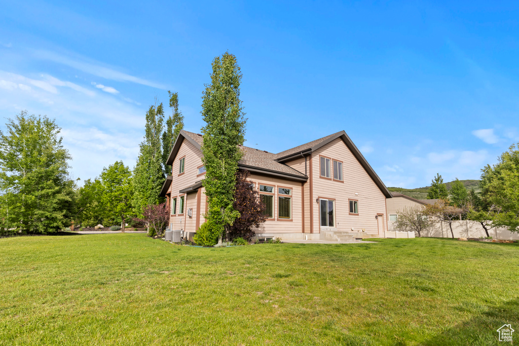 Back of property with central AC, a patio area, and a shingled roof