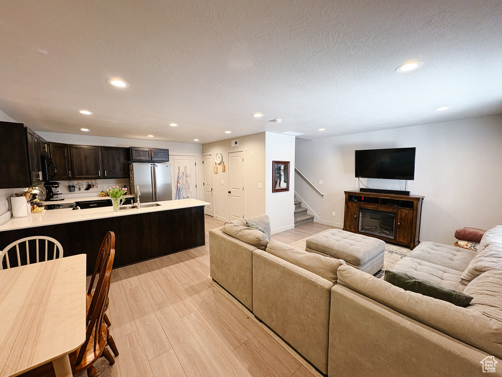 Living room featuring recessed lighting, light wood-style floors, a glass covered fireplace, and stairs