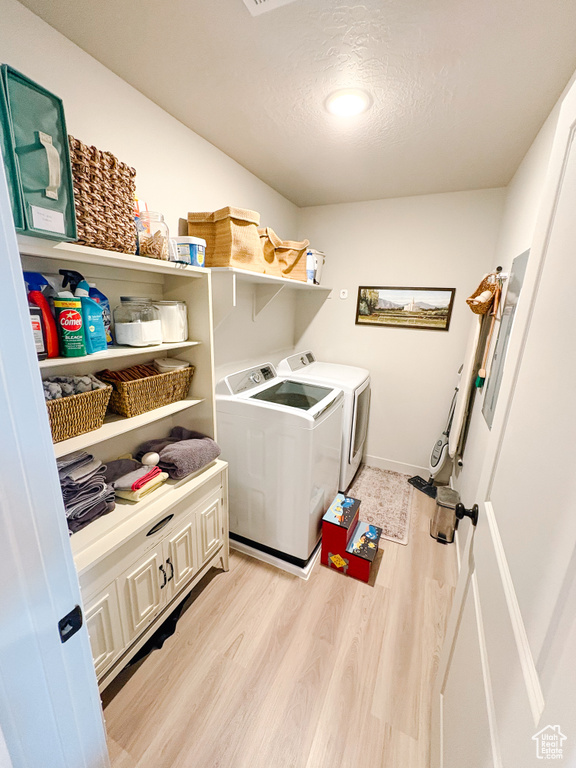 Laundry area with baseboards, laundry area, light wood-style flooring, a textured ceiling, and washing machine and dryer