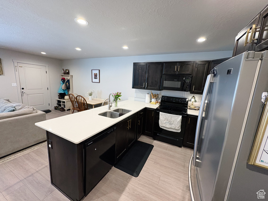 Kitchen with black appliances, a sink, open floor plan, a peninsula, and dark cabinets