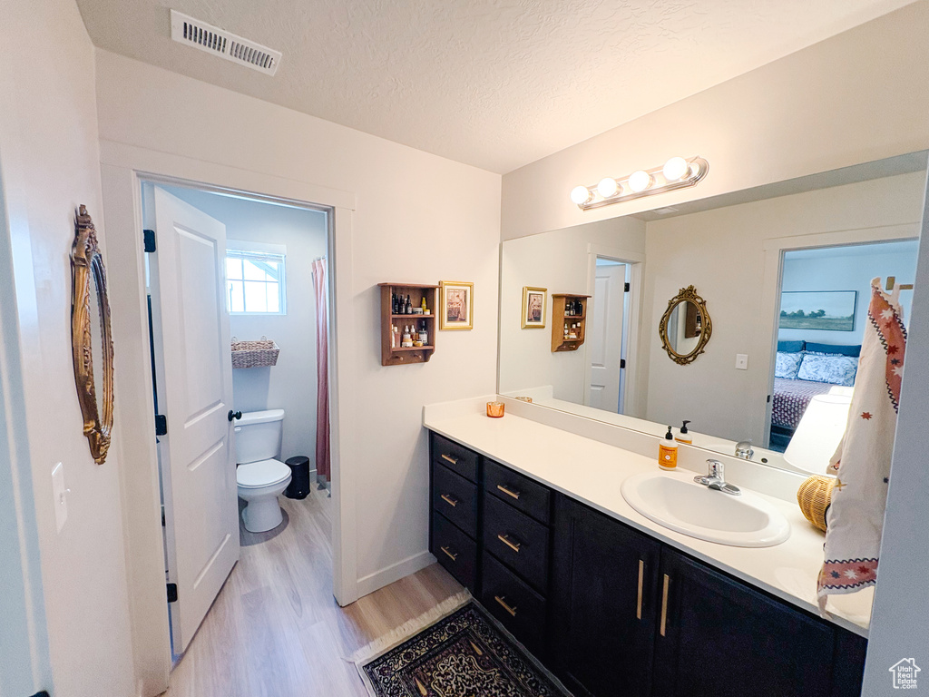 Ensuite bathroom with visible vents, toilet, a textured ceiling, wood finished floors, and vanity