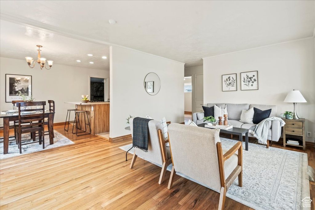 Living area with a chandelier, wood finished floors, baseboards, and ornamental molding