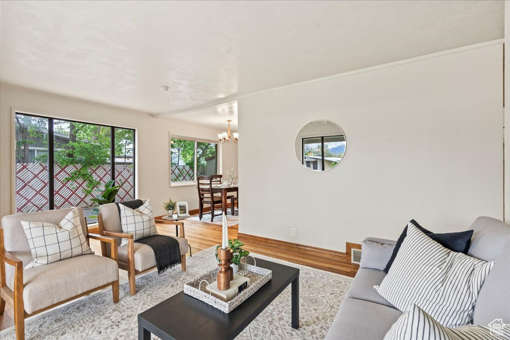 Living room with baseboards, visible vents, crown molding, light wood-style flooring, and a notable chandelier