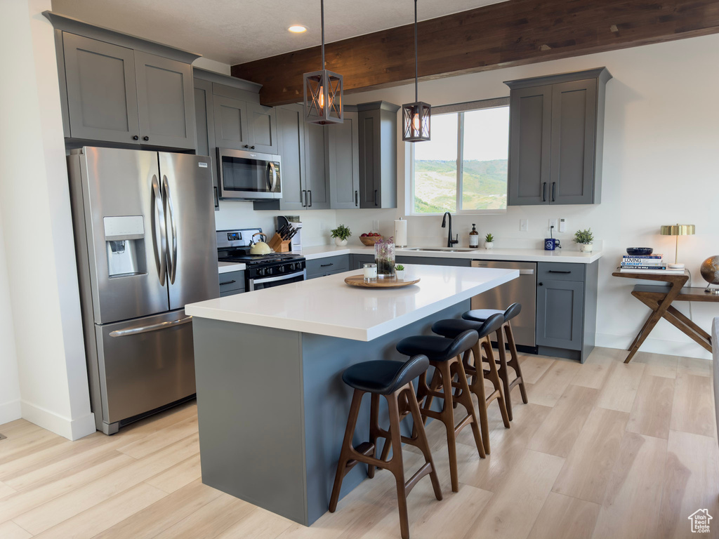 Kitchen featuring light wood finished floors, a sink, appliances with stainless steel finishes, a kitchen breakfast bar, and a center island