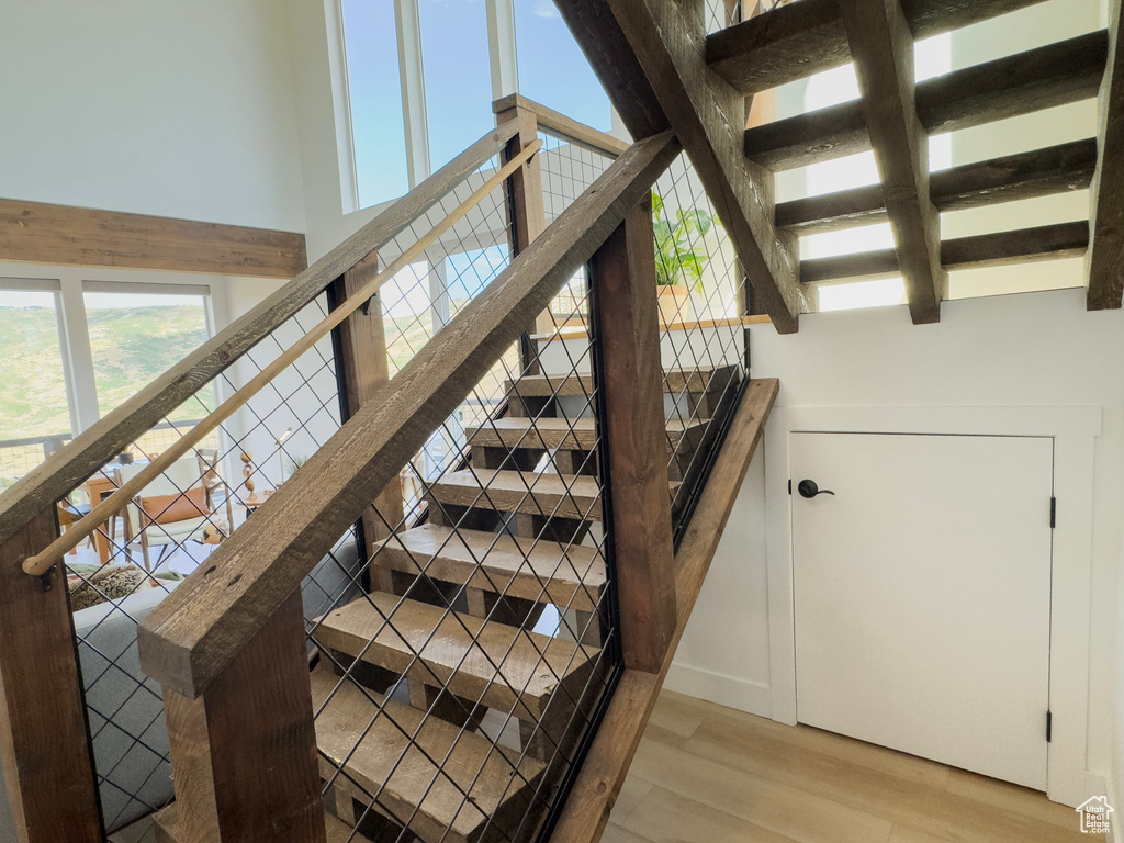 Staircase with a high ceiling, wood finished floors, and beamed ceiling