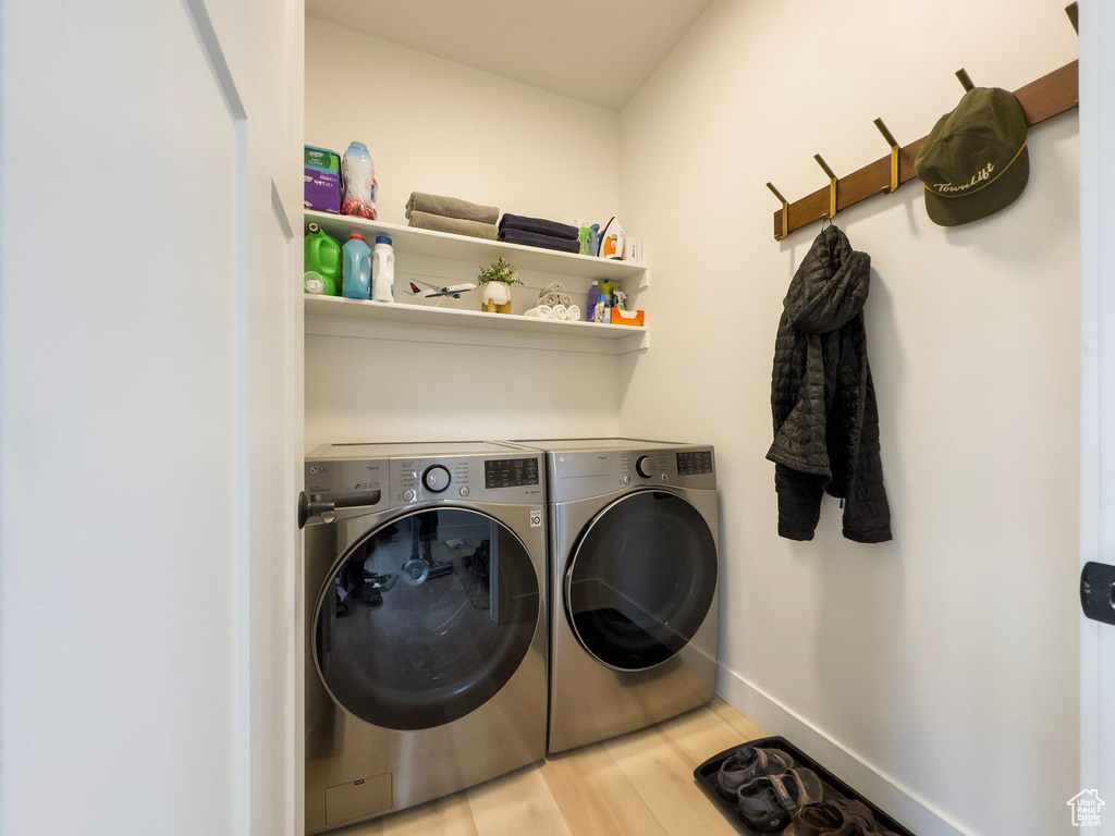 Clothes washing area featuring laundry area, washer and dryer, baseboards, and wood finished floors