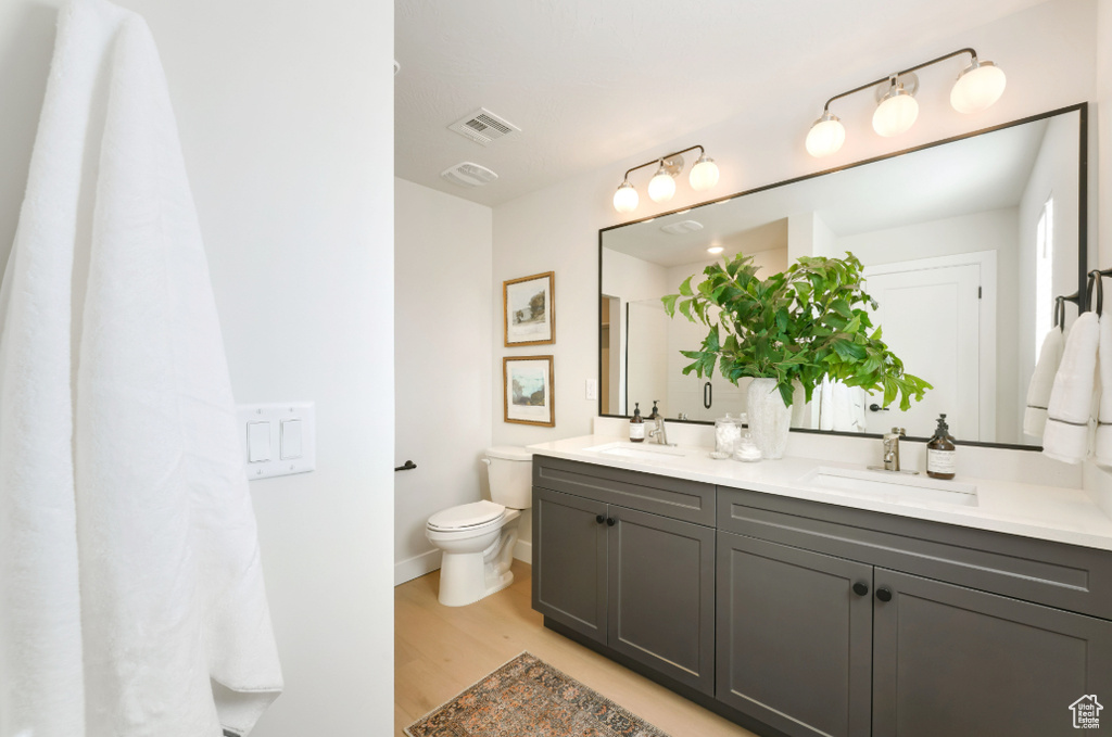 Bathroom with a sink, visible vents, toilet, and wood finished floors