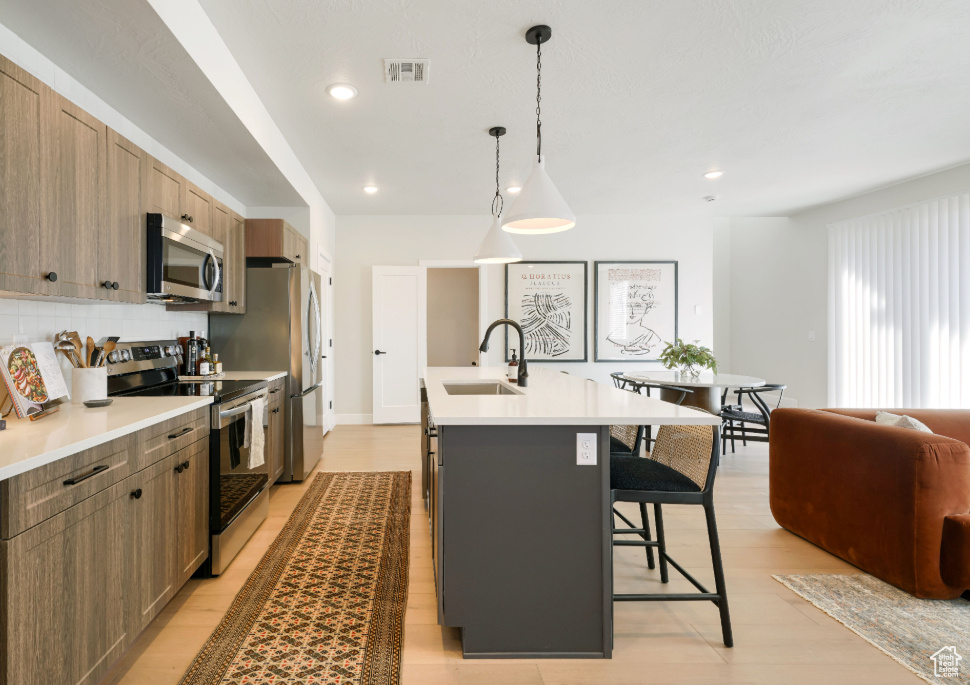 Kitchen featuring visible vents, a center island with sink, a kitchen bar, appliances with stainless steel finishes, and a sink
