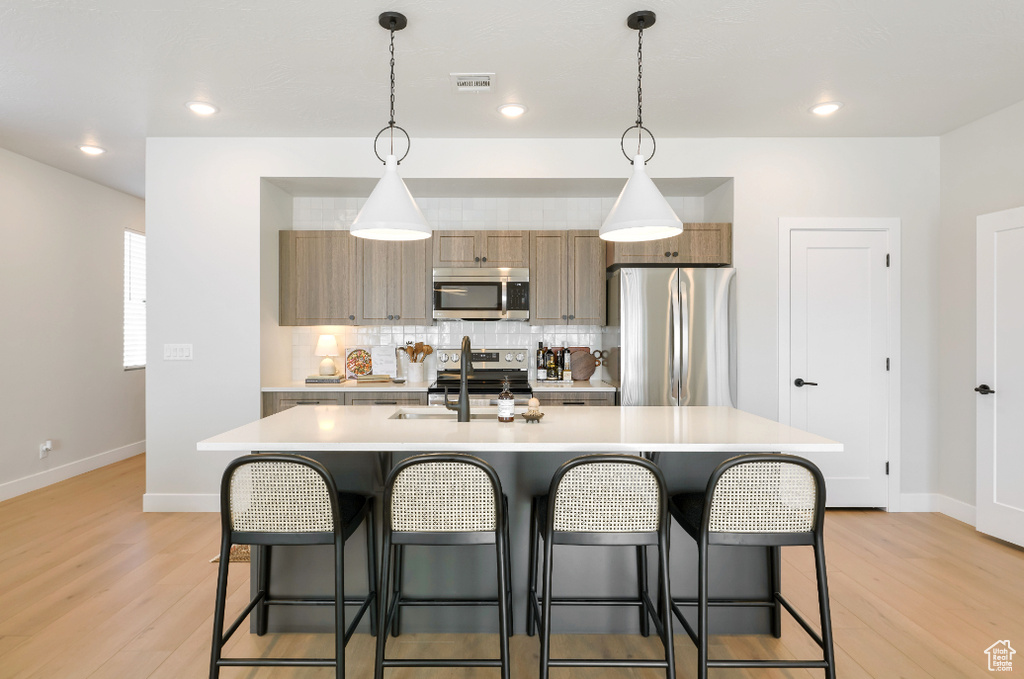 Kitchen featuring visible vents, a sink, decorative backsplash, light countertops, and stainless steel appliances