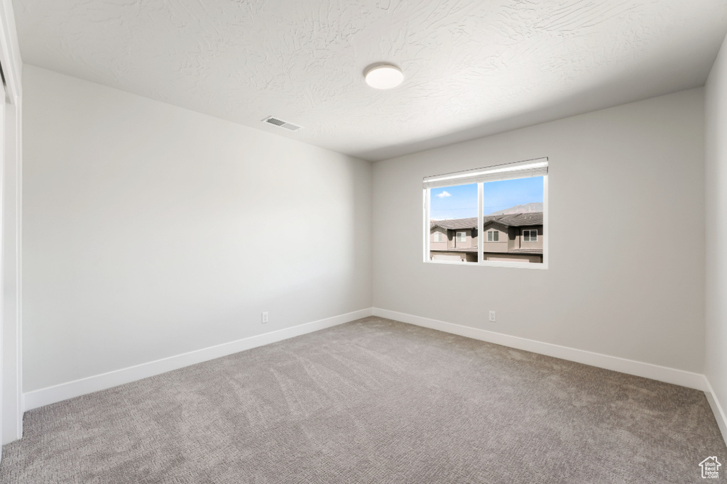 Carpeted empty room featuring visible vents, a textured ceiling, and baseboards