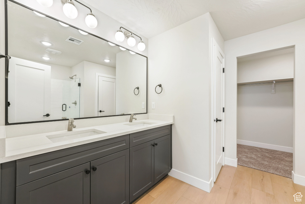 Bathroom with a sink, visible vents, wood finished floors, and a stall shower