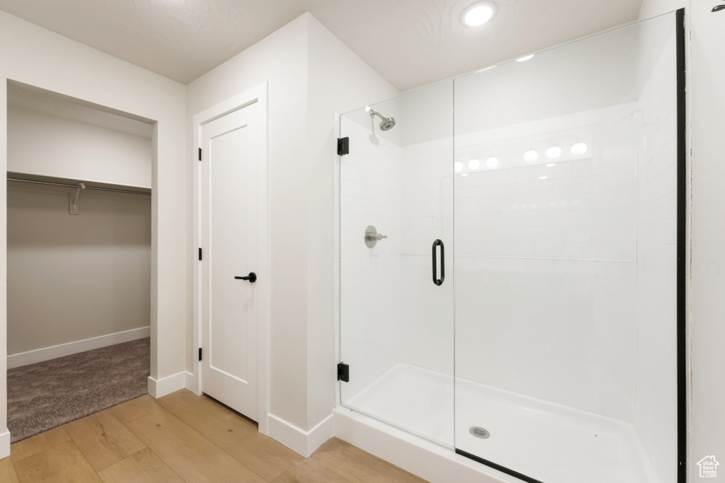 Full bathroom with a walk in closet, wood finished floors, a stall shower, and baseboards