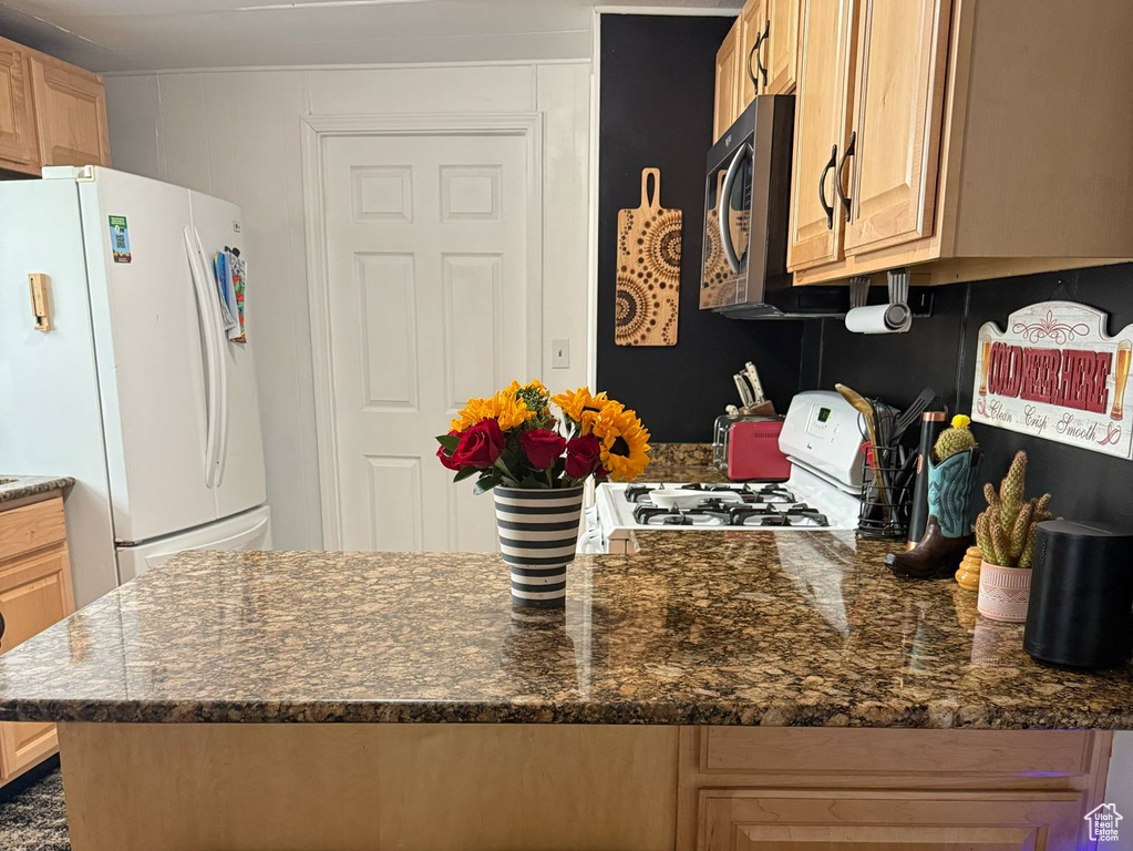 Kitchen with white appliances, a peninsula, a kitchen breakfast bar, and dark stone countertops