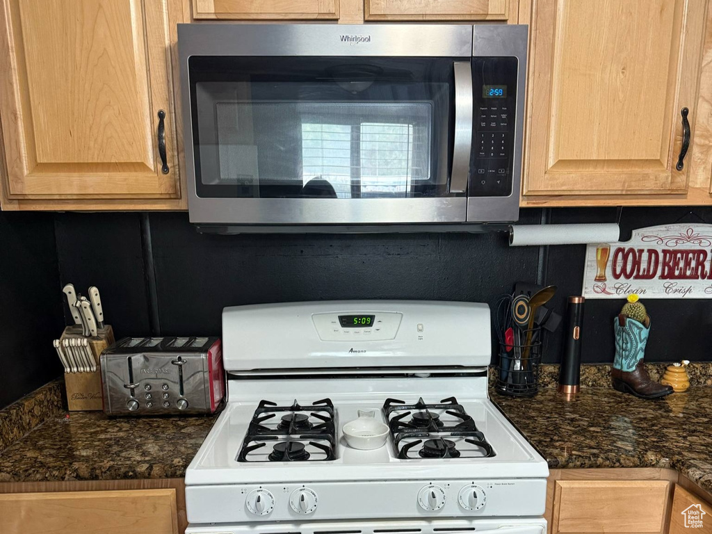 Kitchen featuring stainless steel microwave, white gas stove, dark countertops, and light brown cabinetry