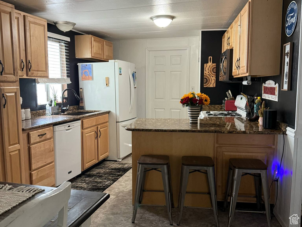 Kitchen featuring white appliances, a peninsula, a sink, dark countertops, and a breakfast bar area