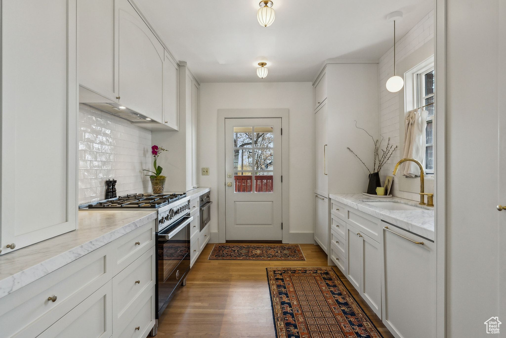 Kitchen with a sink, backsplash, white cabinets, light wood finished floors, and high end range