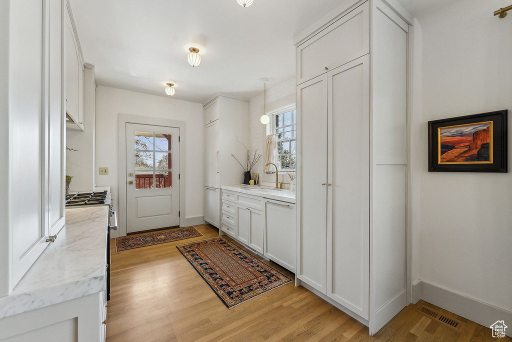 Kitchen with light wood finished floors, visible vents, dishwasher, white cabinetry, and a sink