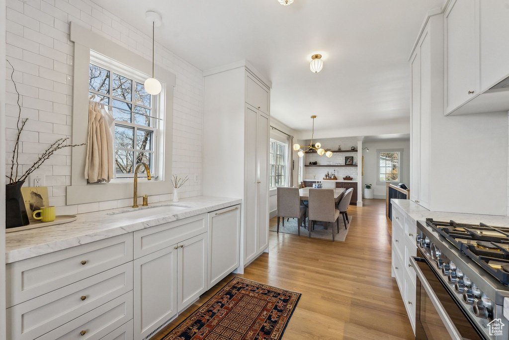 Kitchen featuring white cabinetry, light wood-style flooring, a sink, high end stainless steel range oven, and backsplash