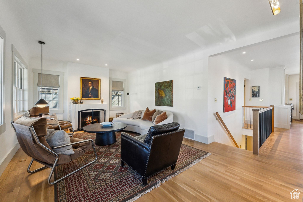 Living room featuring visible vents, light wood-style flooring, a warm lit fireplace, and baseboards