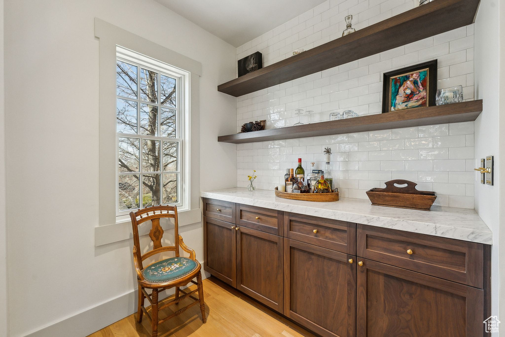Bar featuring tasteful backsplash, plenty of natural light, light wood-style flooring, and baseboards