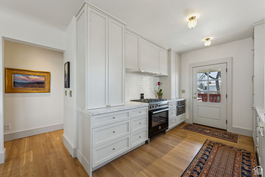 Kitchen featuring backsplash, high end black range oven, white cabinetry, and light wood-style floors
