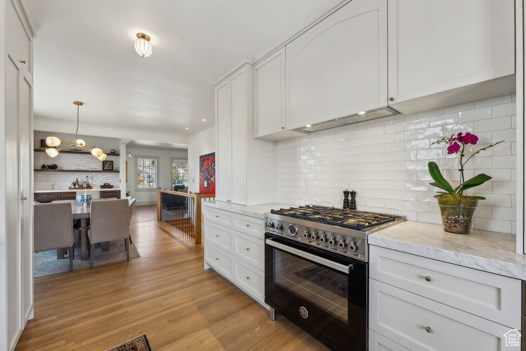 Kitchen with light stone counters, light wood-style flooring, high end stove, white cabinetry, and tasteful backsplash