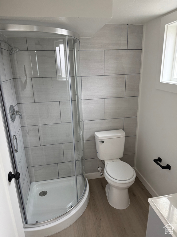 Full bath with toilet, baseboards, wood finished floors, and a stall shower