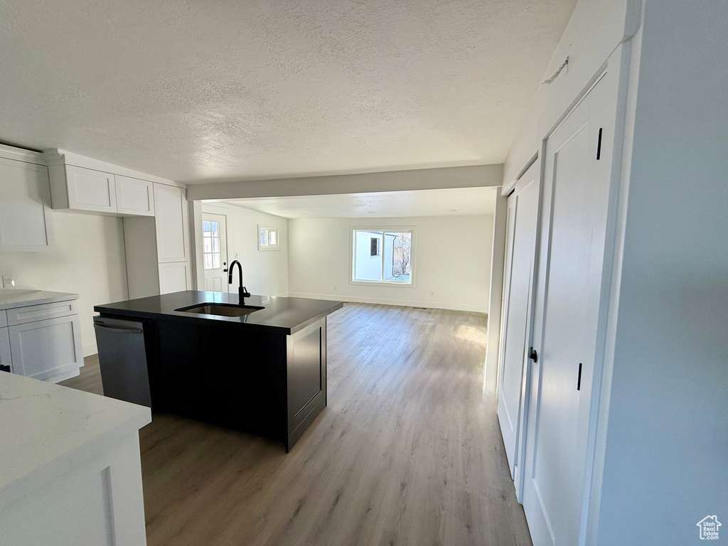 Kitchen with open floor plan, dishwasher, light wood-style floors, a textured ceiling, and a sink