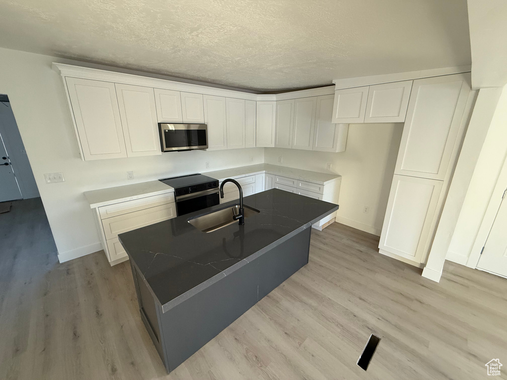 Kitchen featuring an island with sink, light wood-style flooring, appliances with stainless steel finishes, white cabinetry, and a sink