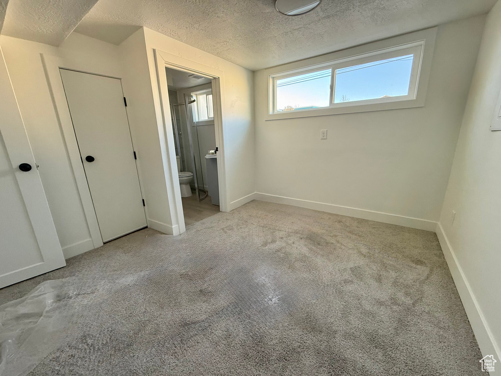 Unfurnished bedroom with ensuite bath, carpet flooring, baseboards, and a textured ceiling