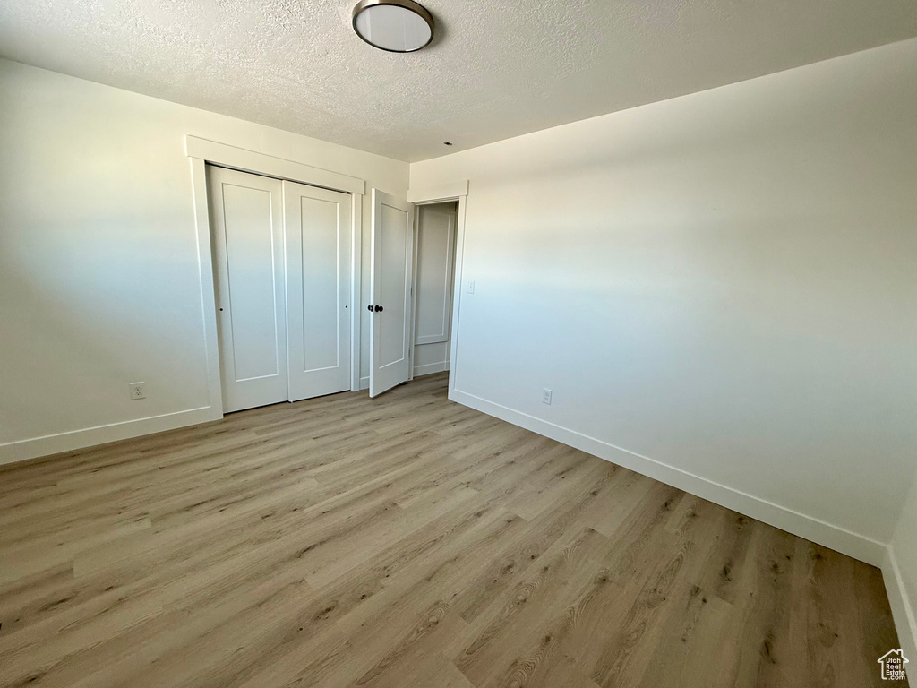 Unfurnished bedroom featuring a closet, a textured ceiling, light wood-type flooring, and baseboards