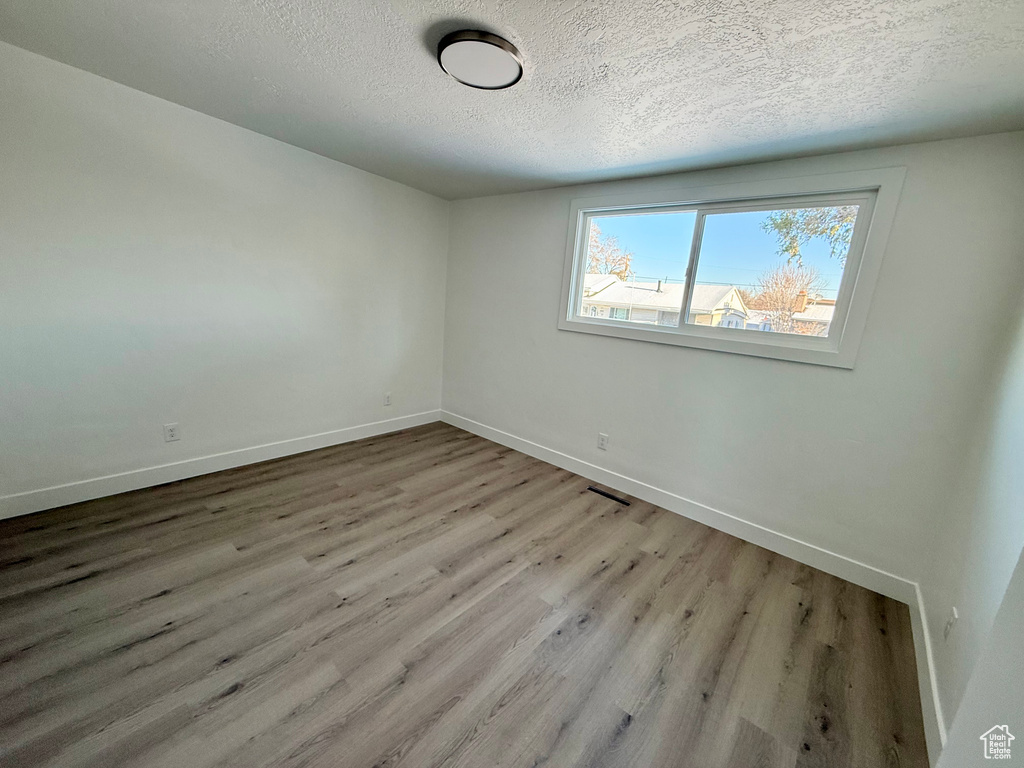 Spare room featuring visible vents, a textured ceiling, baseboards, and wood finished floors