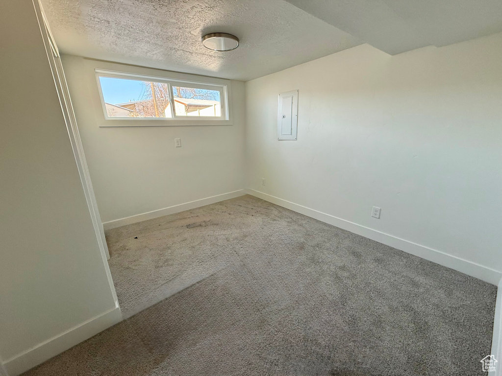 Carpeted spare room with electric panel, baseboards, and a textured ceiling