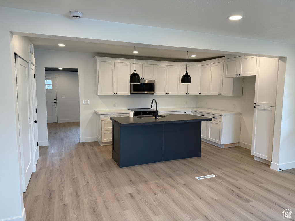 Kitchen with baseboards, recessed lighting, stainless steel microwave, a sink, and light wood-style flooring