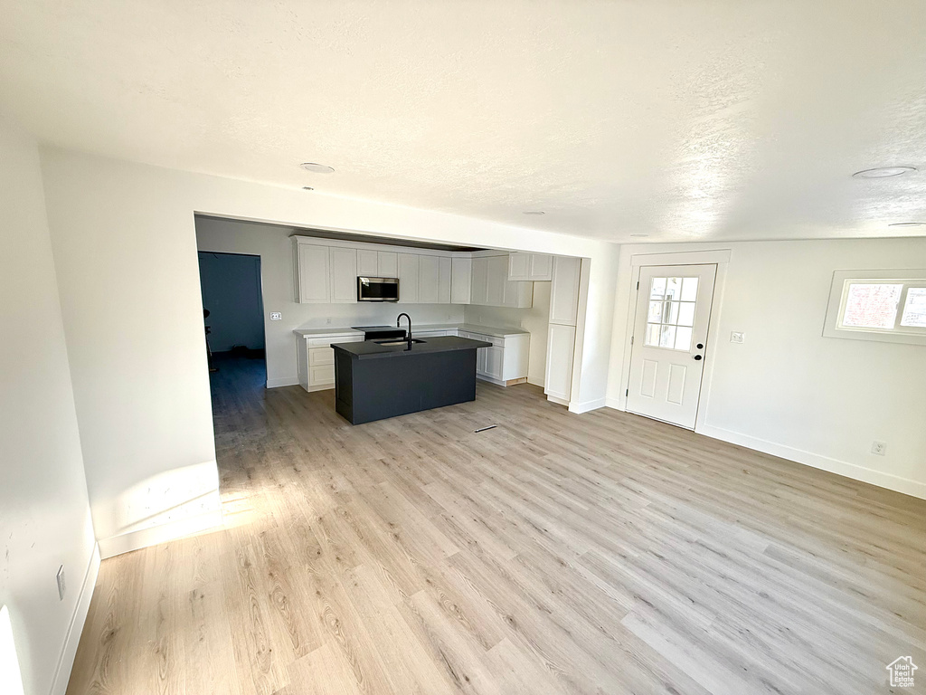 Kitchen featuring a center island with sink, baseboards, light wood-style floors, a textured ceiling, and stainless steel microwave