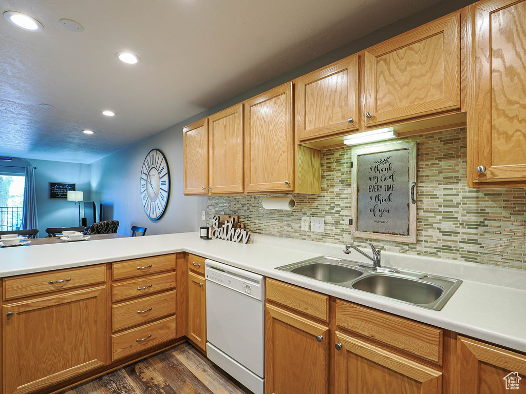 Kitchen with a sink, dishwasher, light countertops, dark wood finished floors, and a peninsula