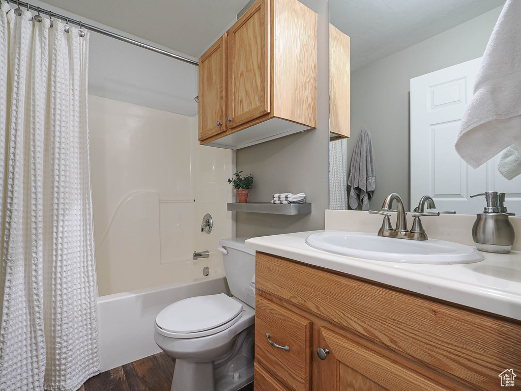 Bathroom featuring toilet, shower / bath combo with shower curtain, wood finished floors, and vanity