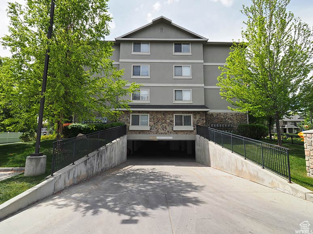 Multi unit property with fence, stone siding, stucco siding, a front yard, and driveway