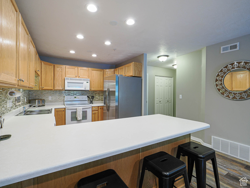 Kitchen featuring a peninsula, decorative backsplash, white appliances, and visible vents
