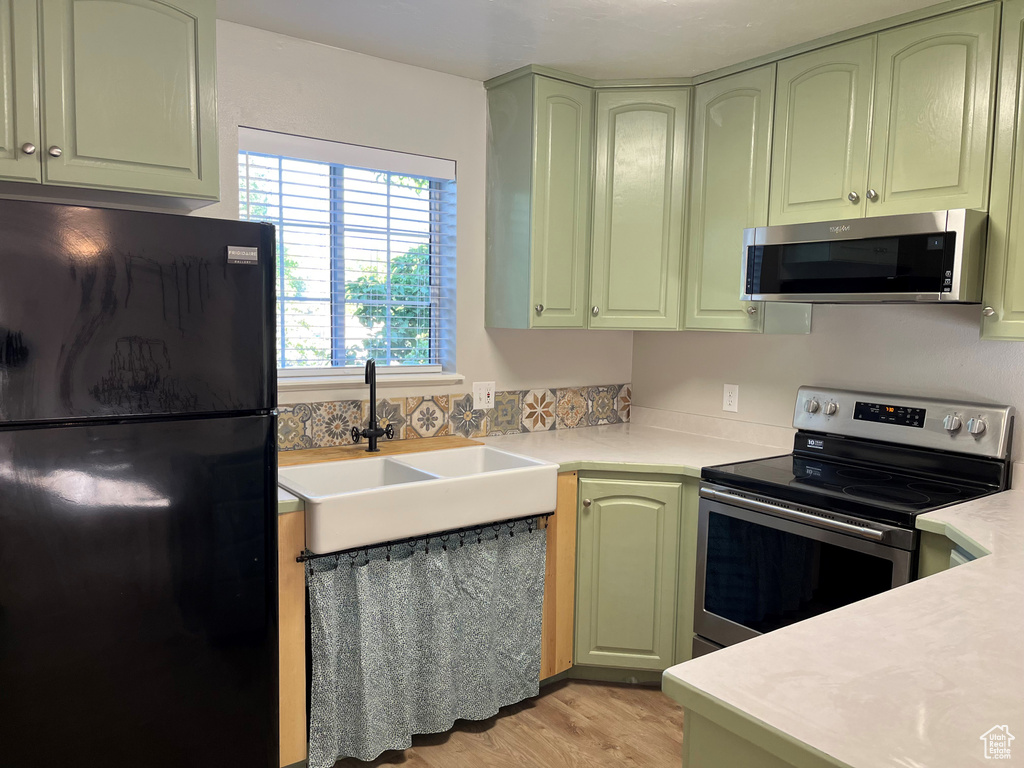 Kitchen with a sink, appliances with stainless steel finishes, green cabinets, and light countertops