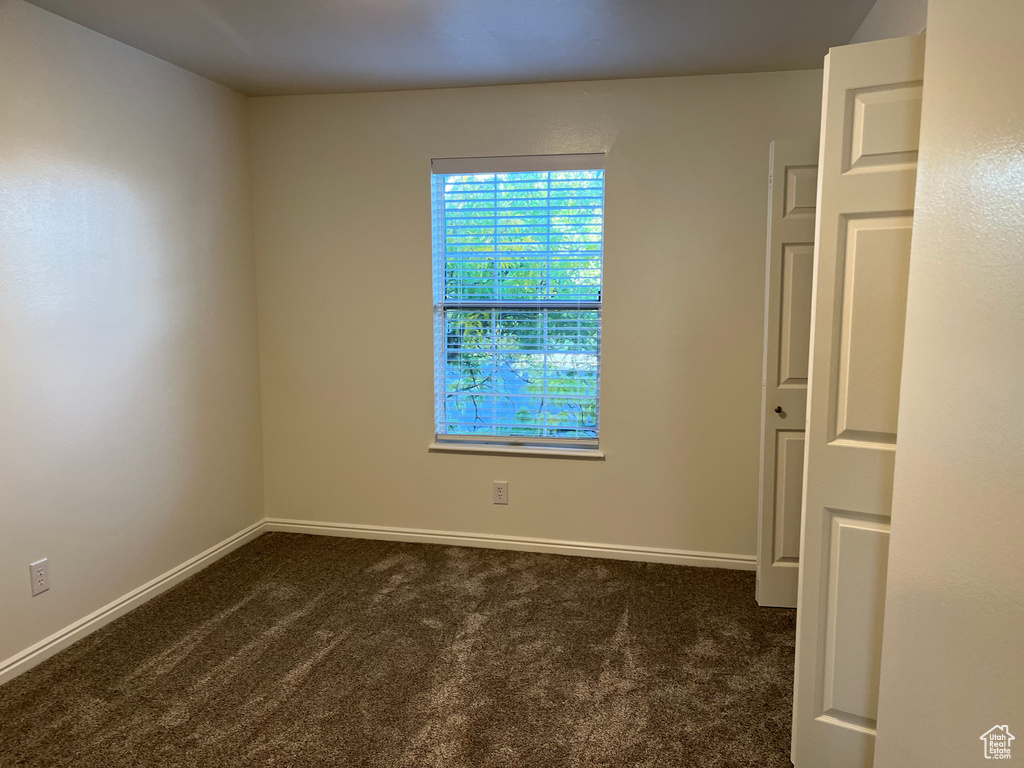 Spare room featuring dark colored carpet and baseboards