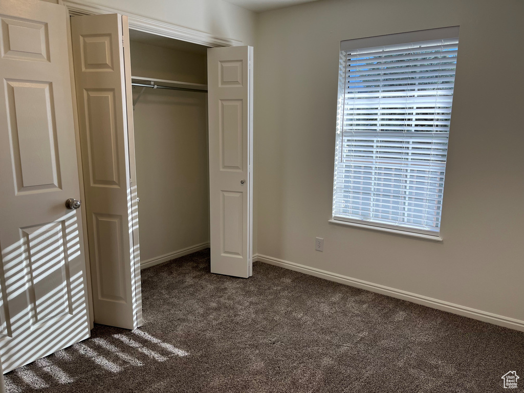 Unfurnished bedroom with baseboards, dark colored carpet, and a closet