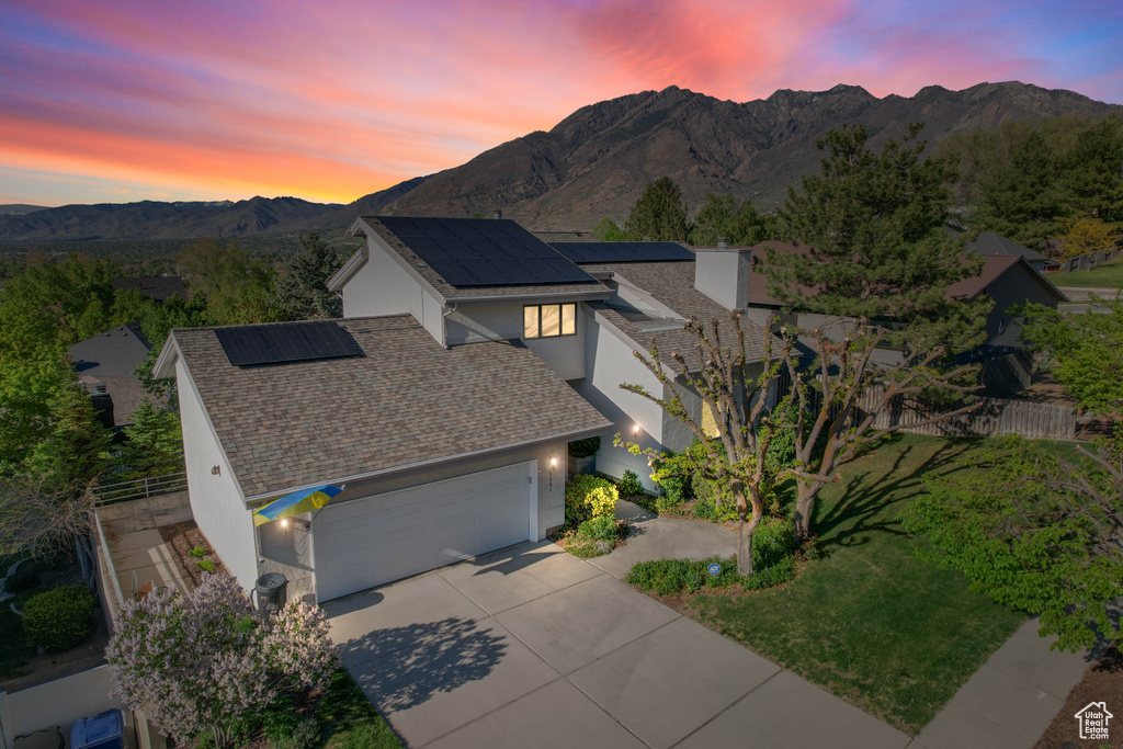Exterior space with a garage, stucco siding, roof mounted solar panels, a mountain view, and concrete driveway