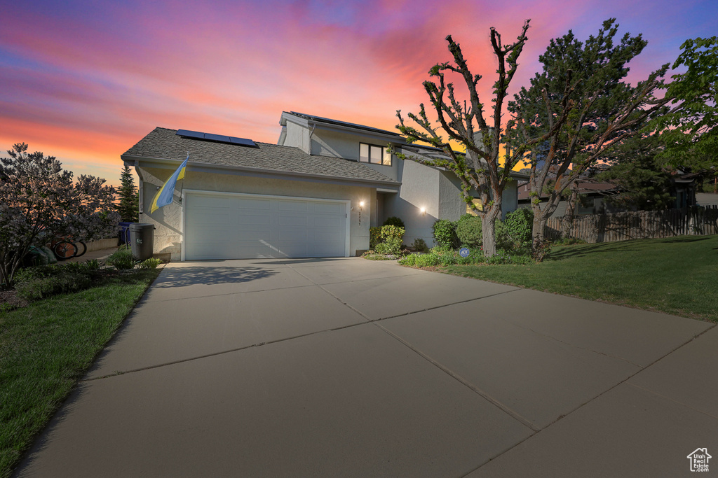 View of front of home with driveway, a garage, roof mounted solar panels, a yard, and stucco siding