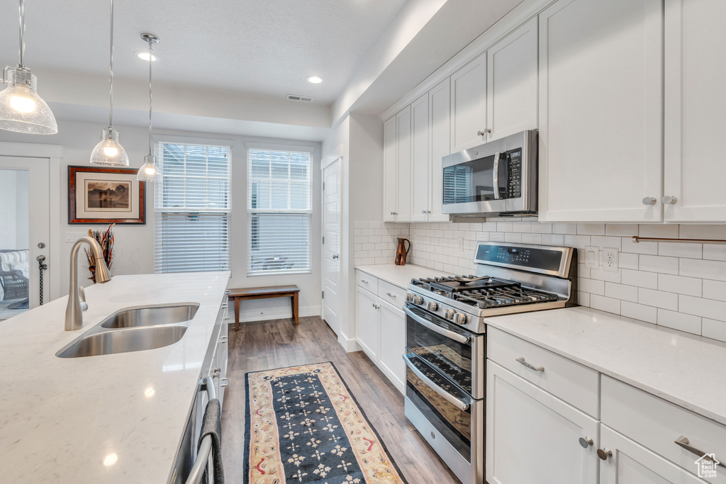 Kitchen with visible vents, a sink, stainless steel appliances, light wood-style floors, and decorative backsplash